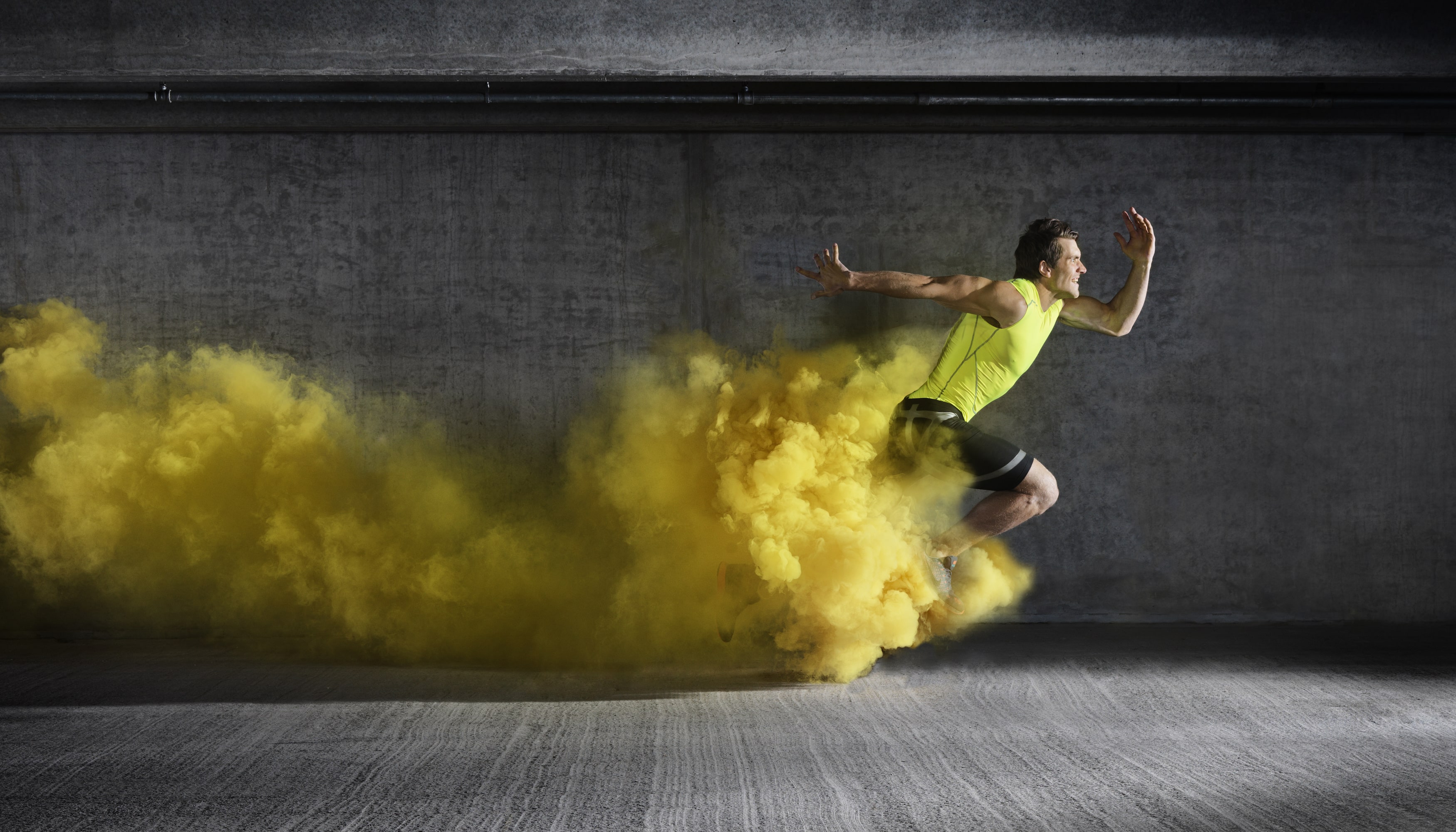 A runner in a yellow vest leaping forward, trailing a cloud of yellow powder