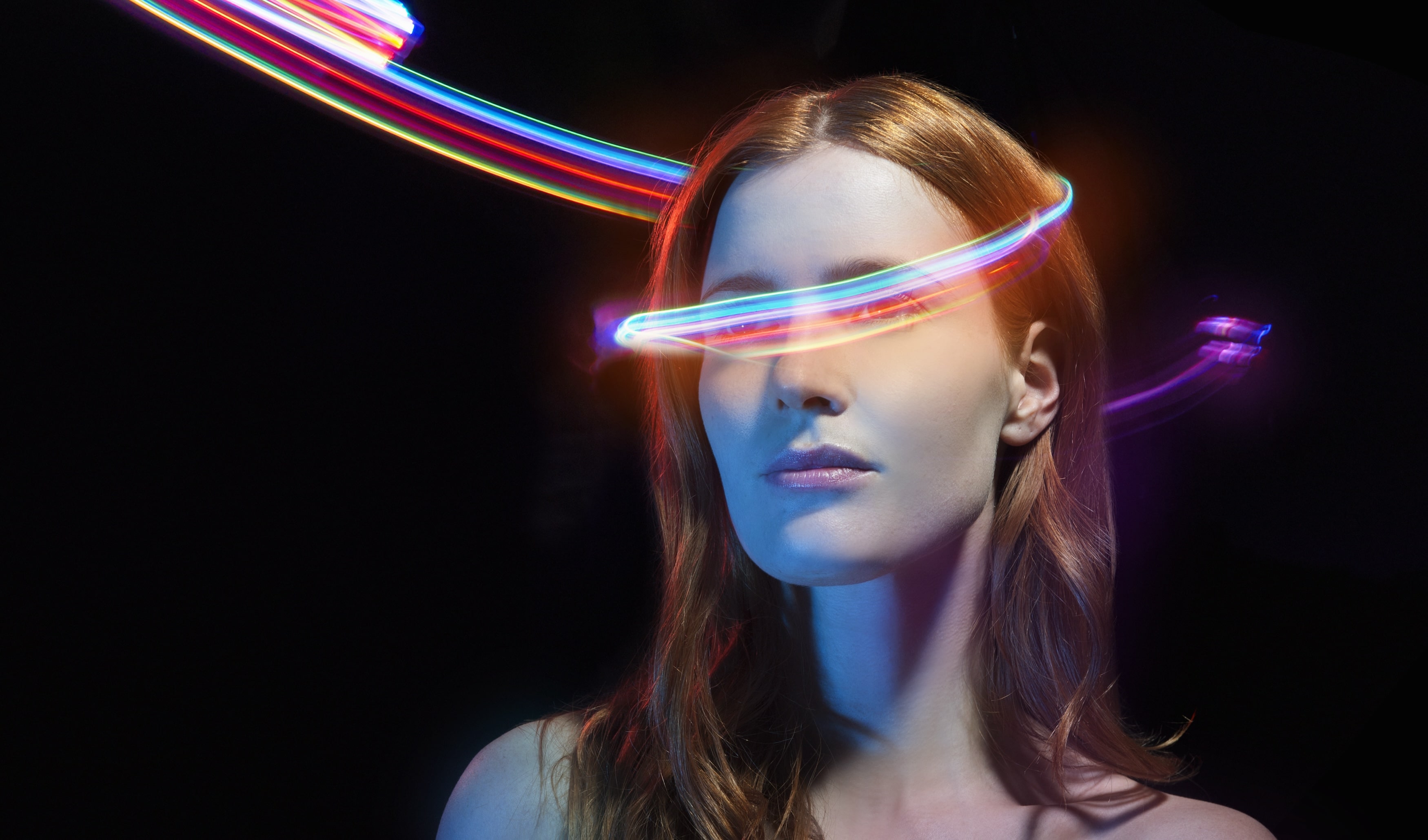A woman wearing a glowing visor, streaks of coloured light arcing over her head