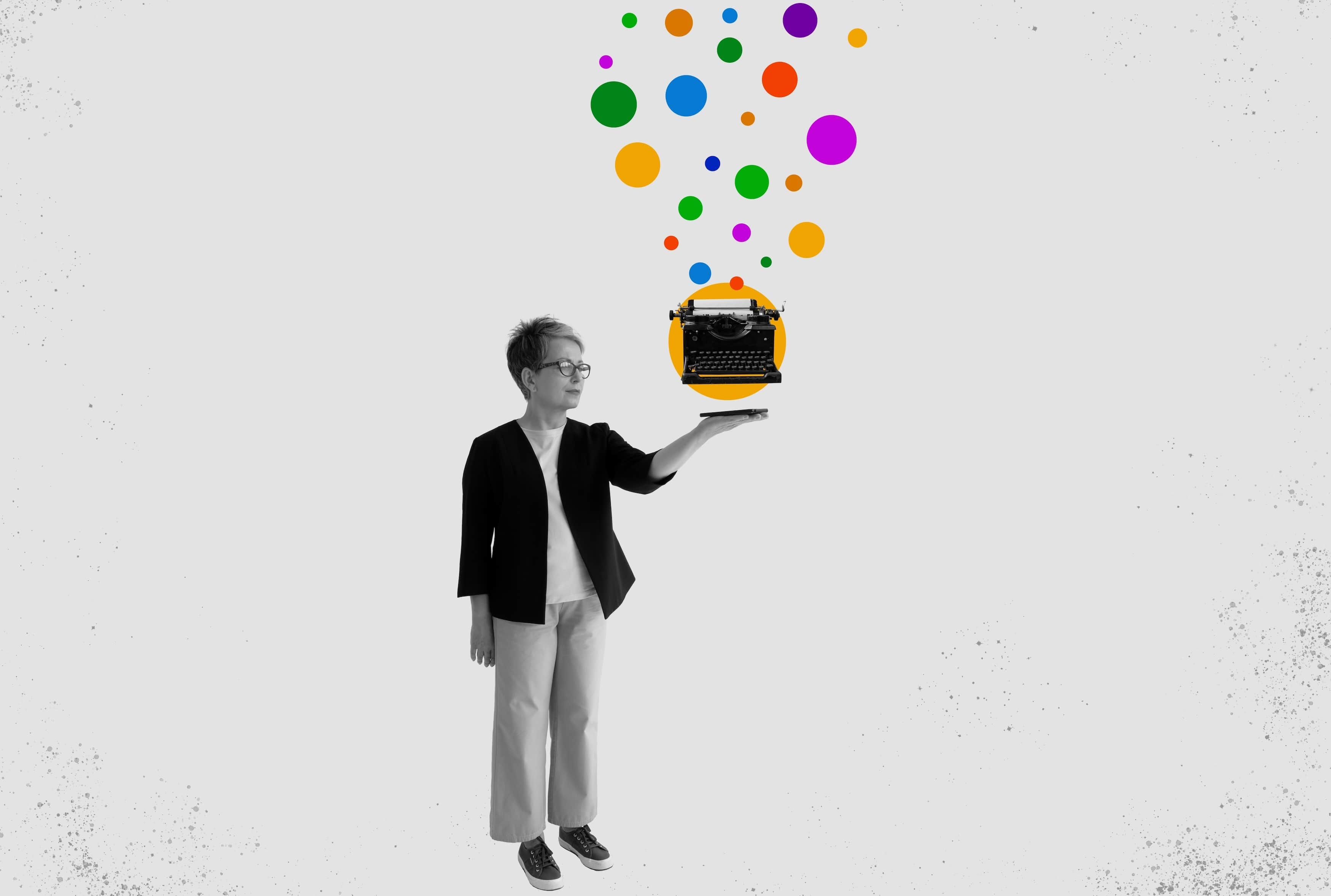 A woman holding out a yellow typewriter with a burst of coloured dots rising from it