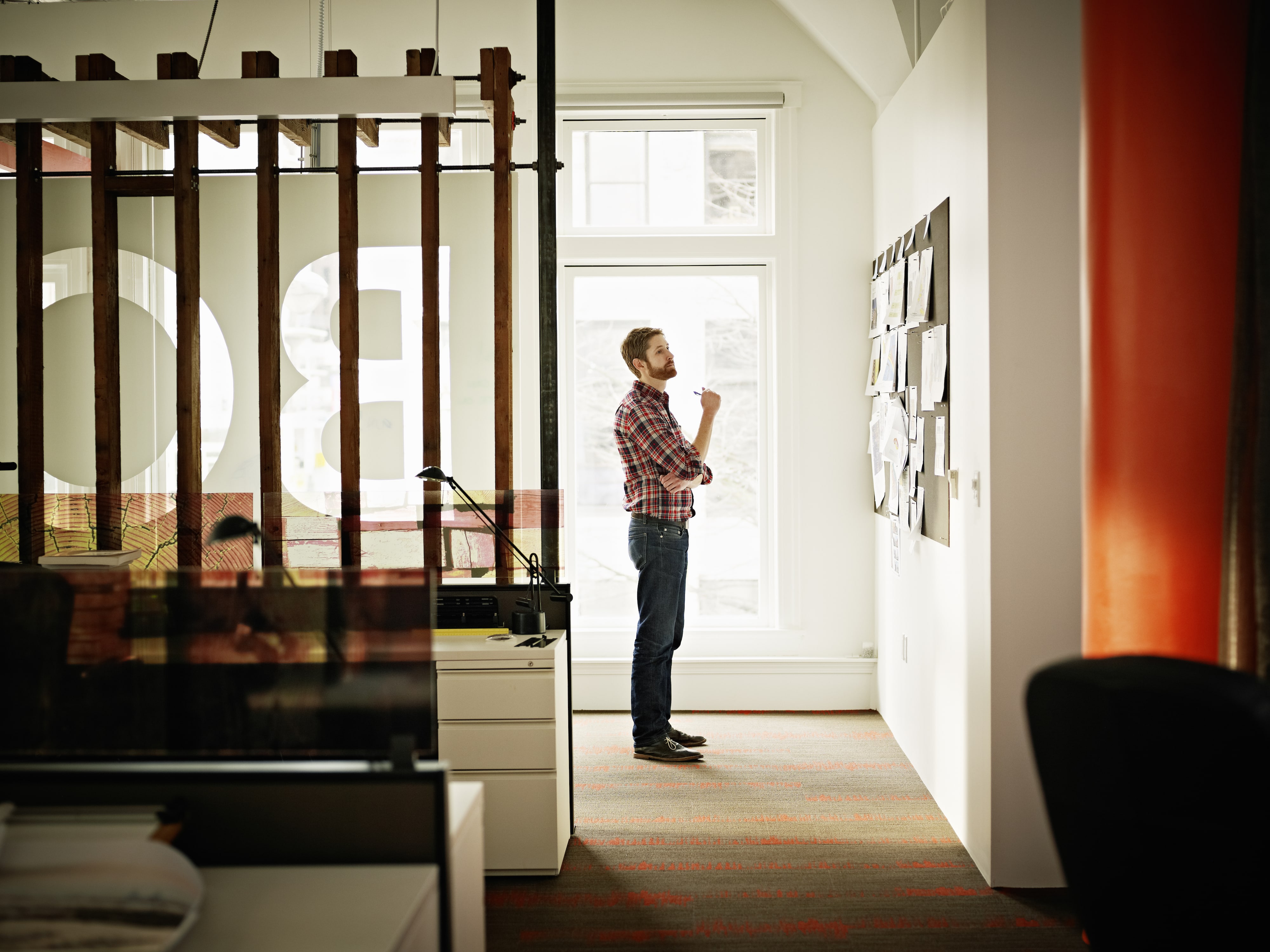 A man standing in an office corridor reading papers pinned to the wall