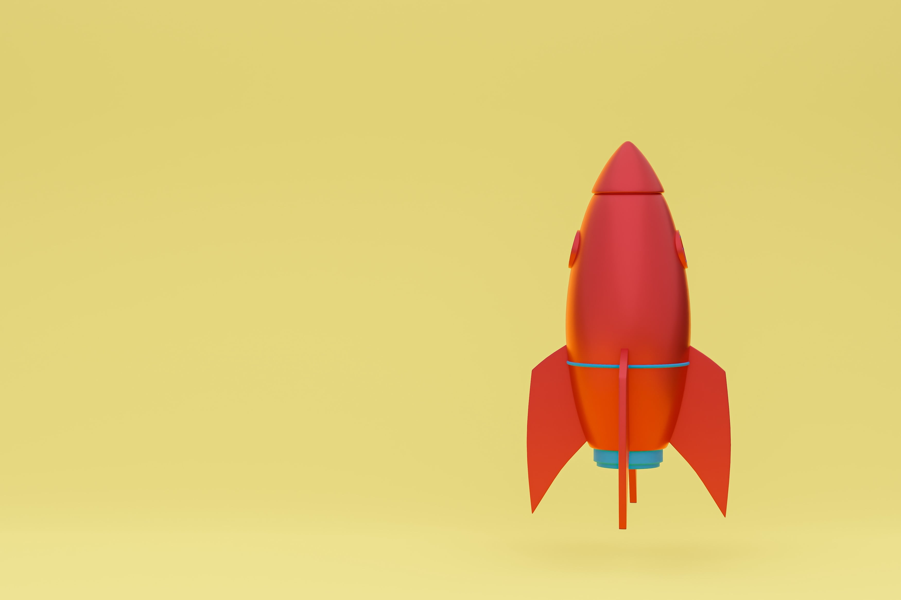 A red toy rocket standing upright on a pale yellow background