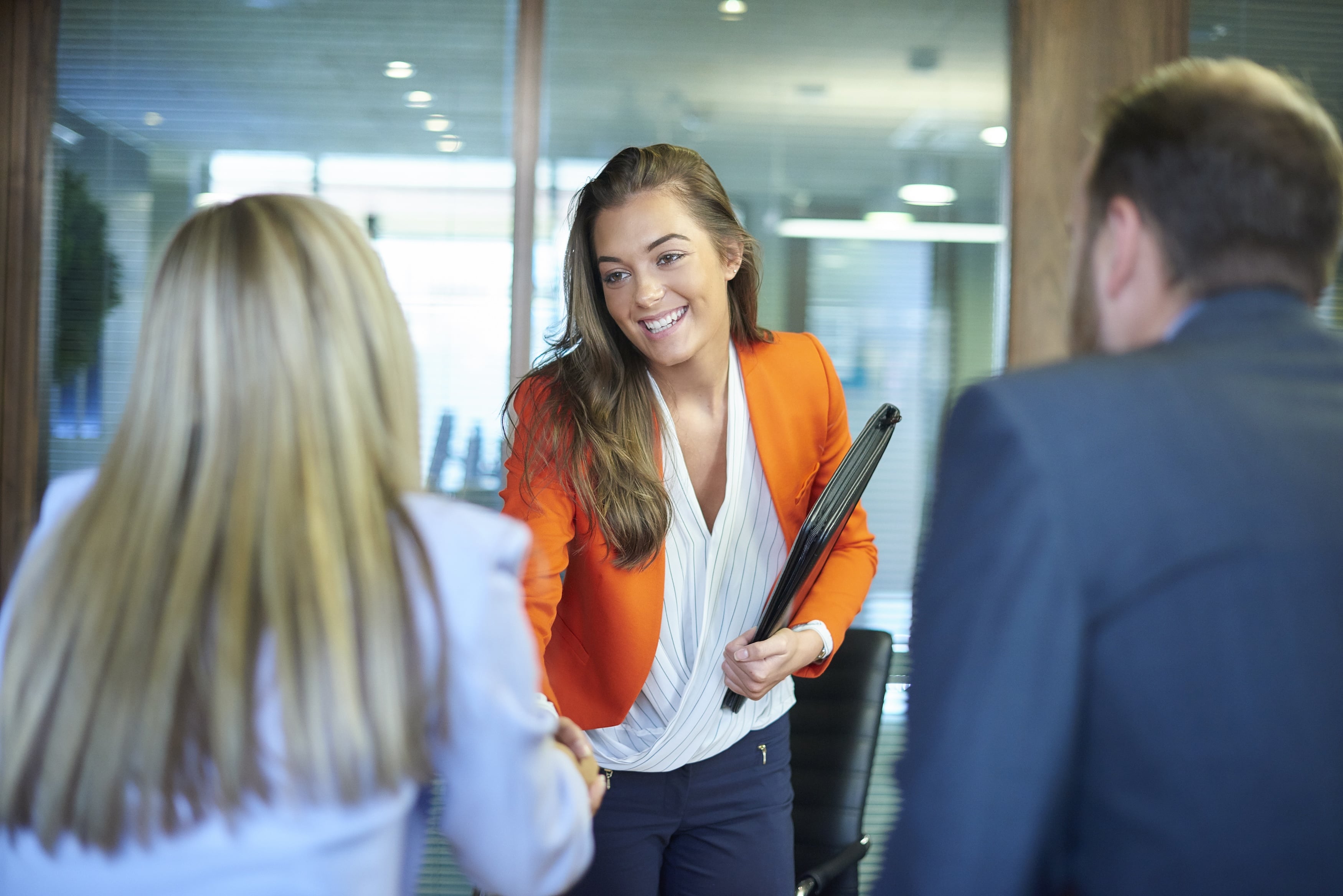 Three colleagues talking in an office, one holding a folder and smiling