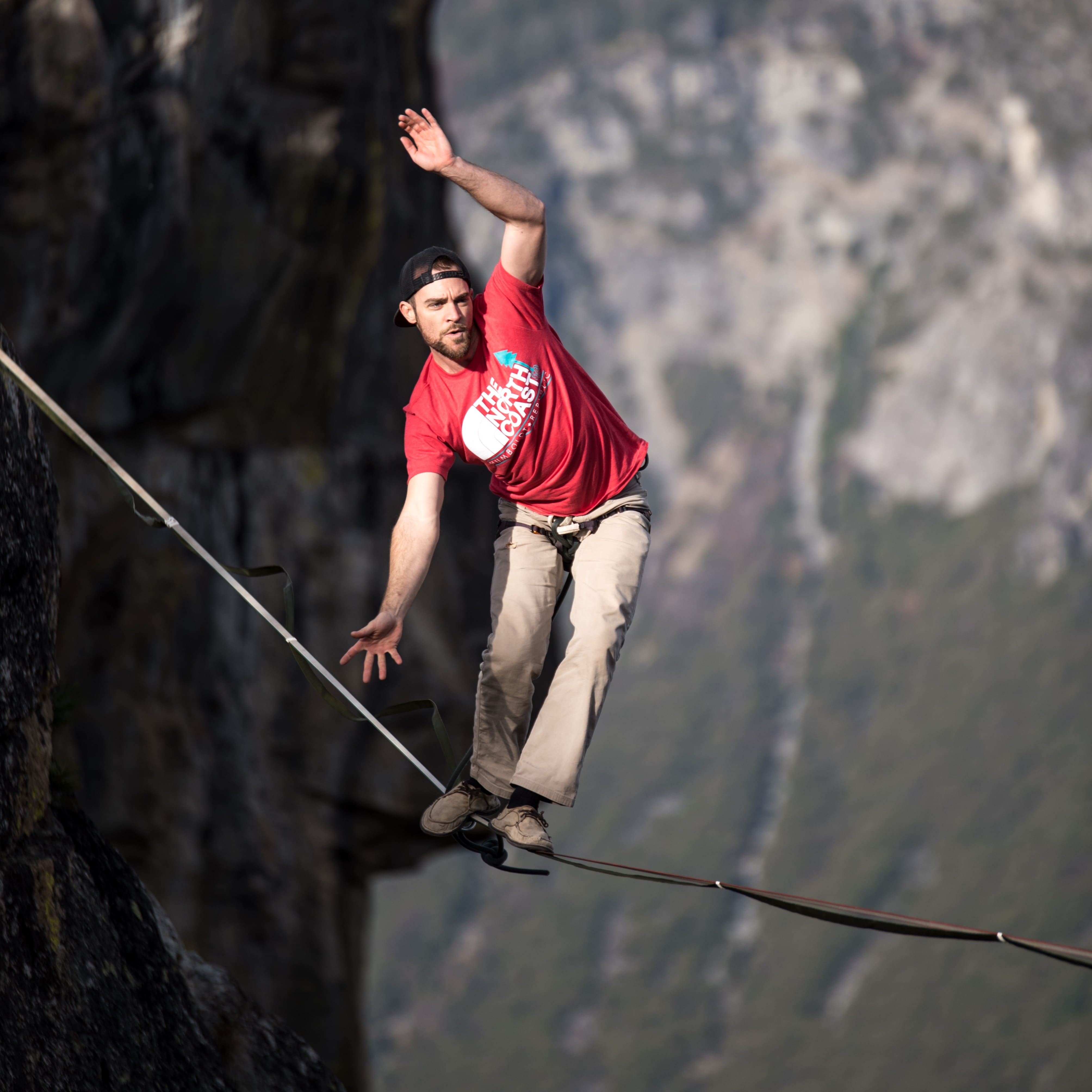 A man walking a slackline strung across a rocky gorge