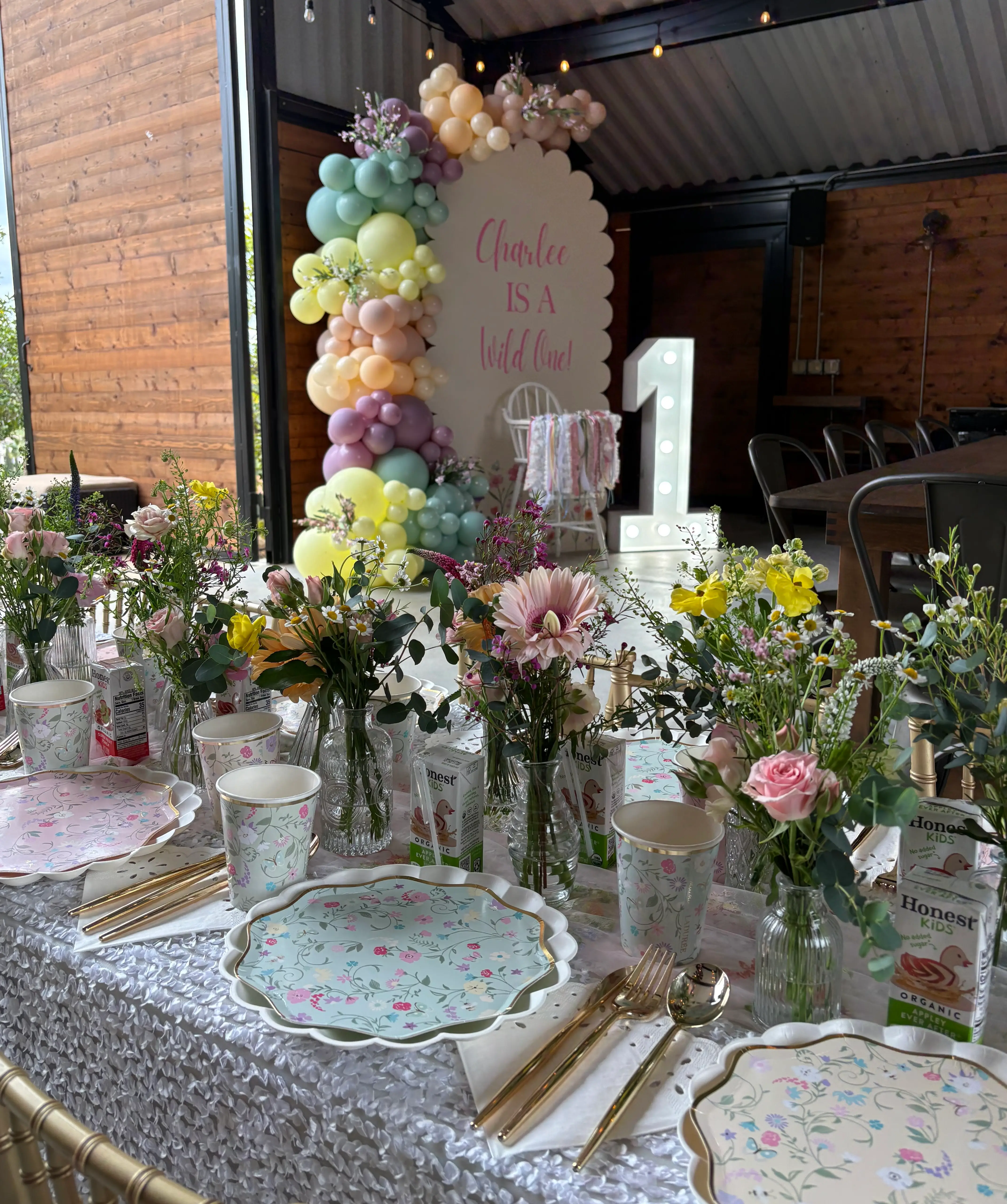 Floral kids birthday table setup with pastel balloon backdrop and custom first birthday decor in Inland Empire