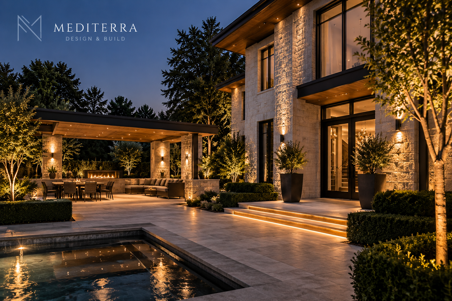Luxurious modern outdoor patio at dusk with illuminated steps, a covered seating area with a fireplace, dining table, and well-lit trees and shrubs.