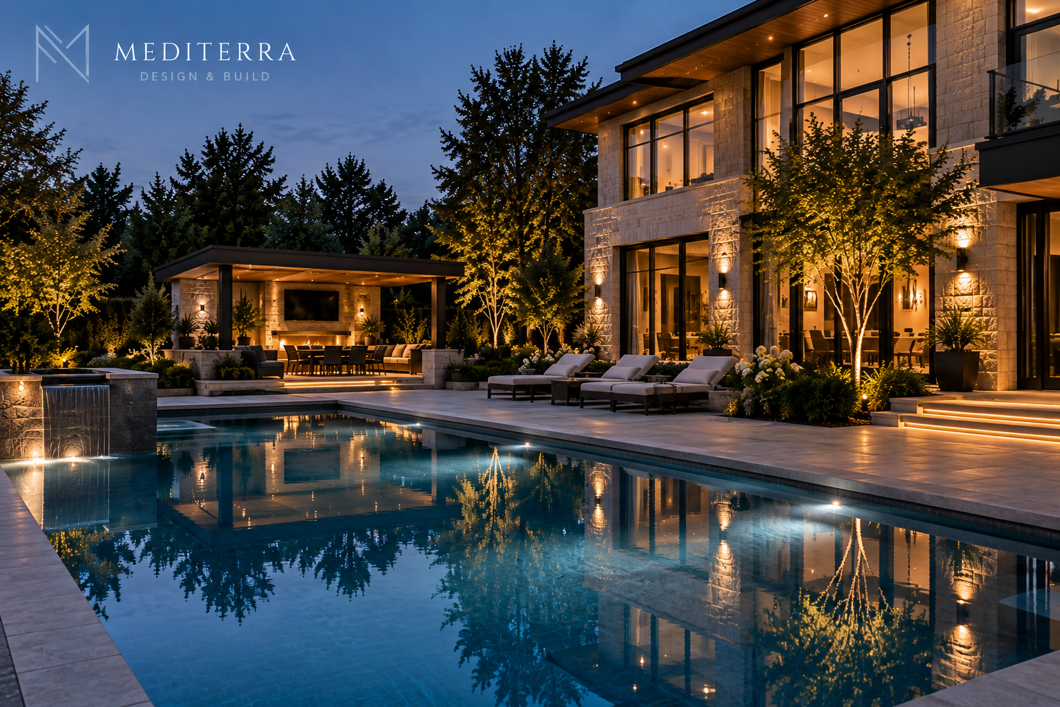 Evening view of a modern luxury home with large windows and an illuminated outdoor pool reflecting the house and surrounding trees, beside a covered patio area with seating, dining table, TV, and warm lighting.