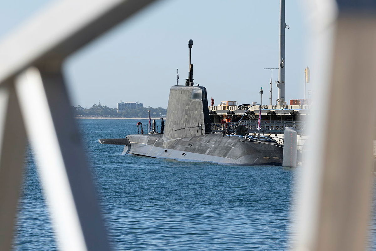 Submarine berthed at a defence facility, viewed through dock infrastructure