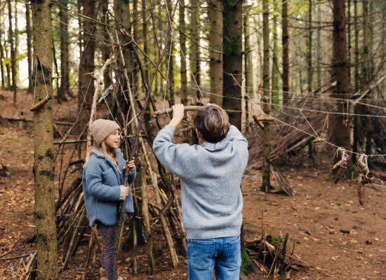 Two siblings on a family holidays builing a tree hut as an autumn DIY at Nutchel
