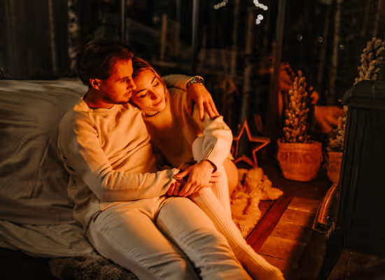 A couple hugging in front of the woodstove of their cabin in the woods during a last-minute holiday at Nutchel