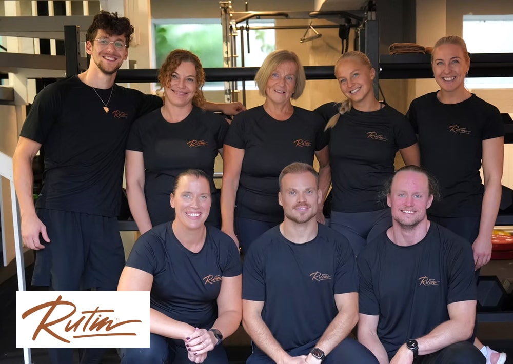 Grupp på åtta personer i svarta Rutin-tröjor poserar tillsammans på gymmet.