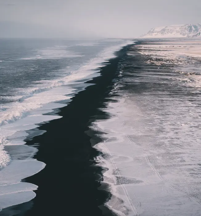 Aerial view of a scenic coastline with waves meeting a snowy shore.