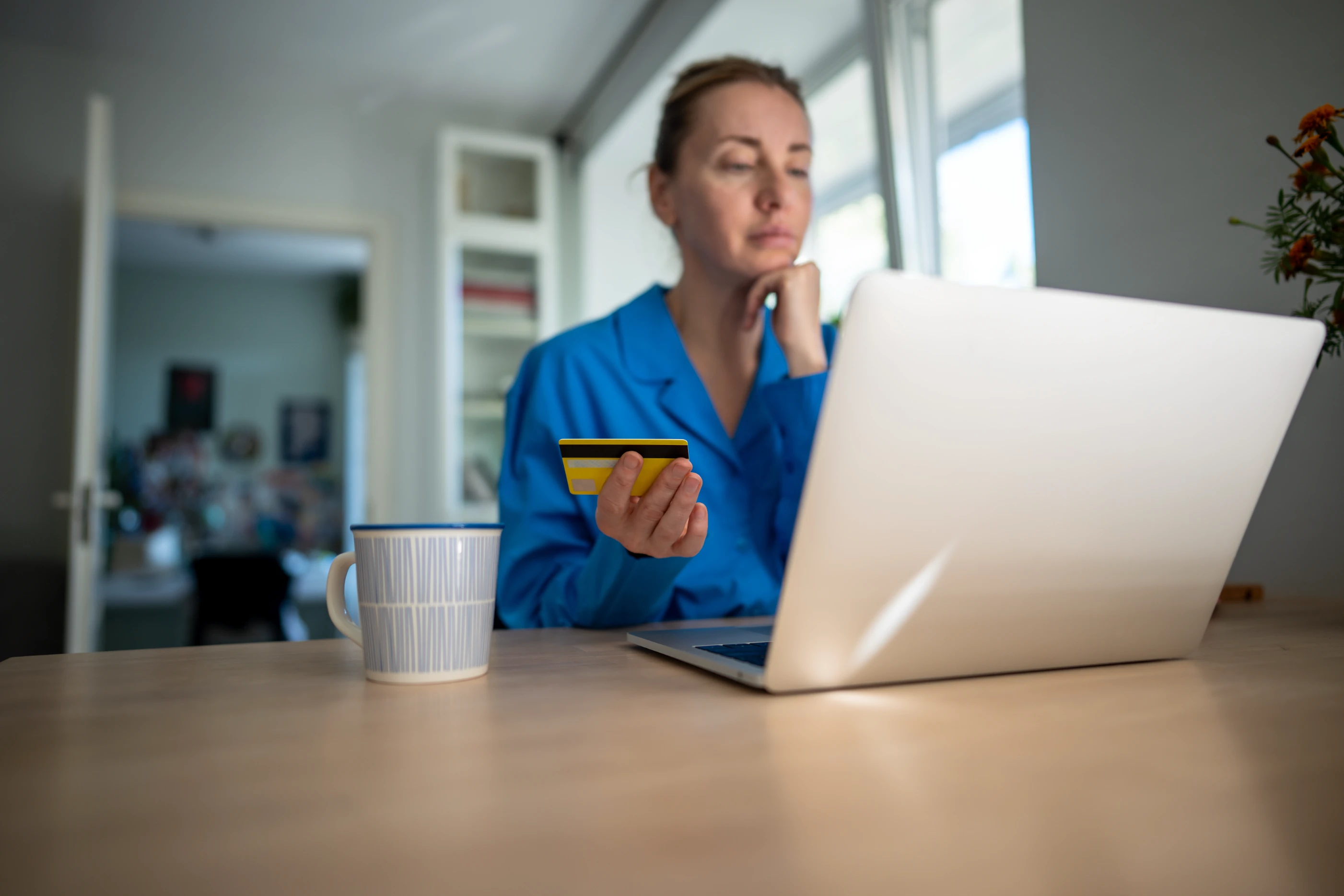 A woman sitting at her laptop with a credit card, about to make an impulsive purchase.
