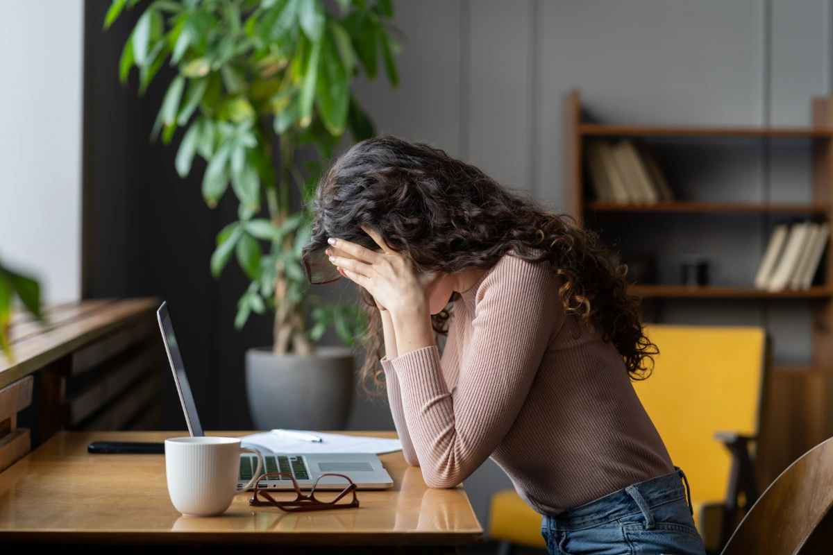 .A woman sitting in front of her laptop hunched over with her head in her hands