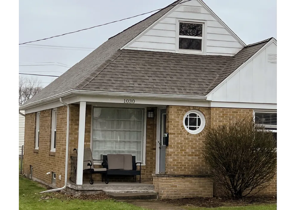 Small brick house with gray shingle roof, white trim, and a porch with outdoor seating.