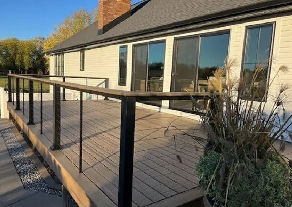 Spacious wooden deck with black metal railing attached to a light-colored house with large windows, under a clear blue sky.