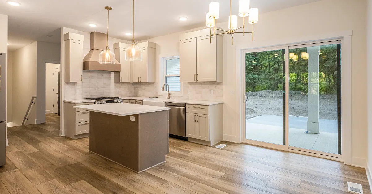 Modern kitchen with beige cabinetry, stainless steel appliances, central island, and sliding glass door leading to outdoor area.