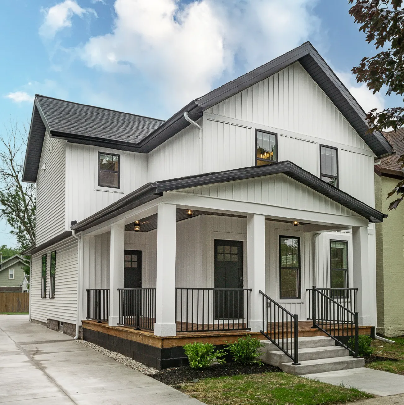Two-story white house with black roof and black-framed windows, featuring a covered porch with black railings and concrete steps.