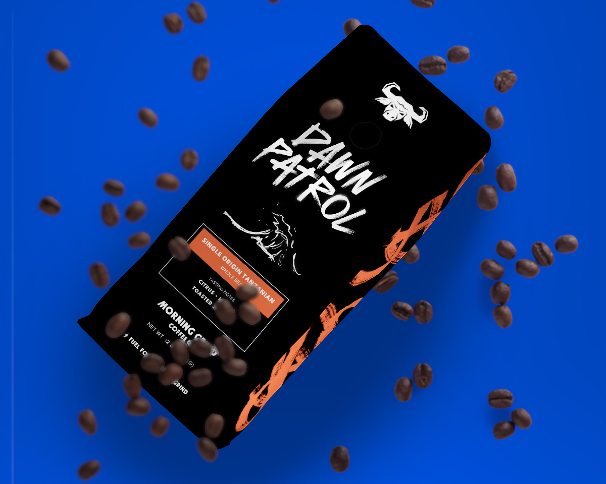 A black coffee bag with the words Dawn Patrol written in an energetic brush stroke font on the front. Also on the front of the bag is a sketchy looking hand drawn illustration of a wave. The sides of the bag are black with red orange scribbles. The bag is against a royal blue background with scattered coffee beans falling all around it. 