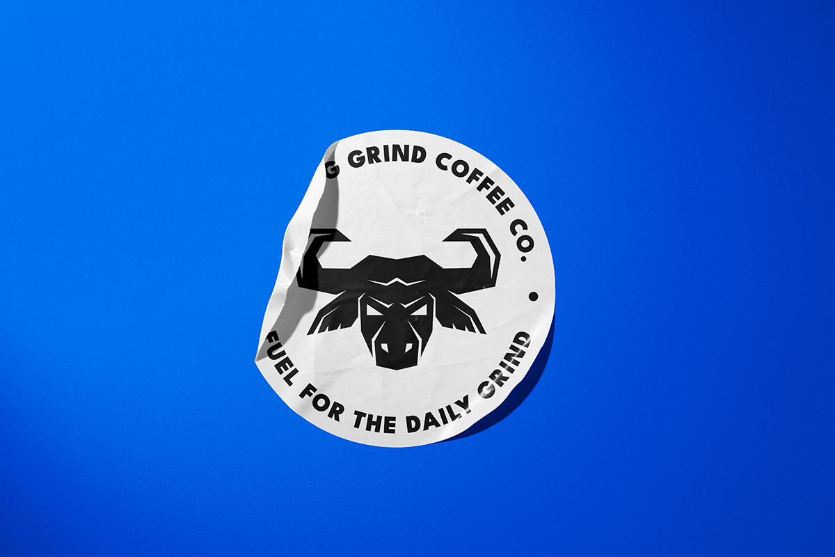 A round, white paper sticker on a royal blue background. On the sticker is an angular geometric logo of a bull head. Around the edge of the sticker are the words Morning Grind Coffee Fuel For The Daily Grind