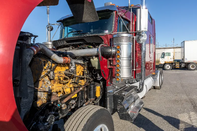 Semi truck engine inspection showing a worn yellow CAT engine with the hood raised in a repair yard.