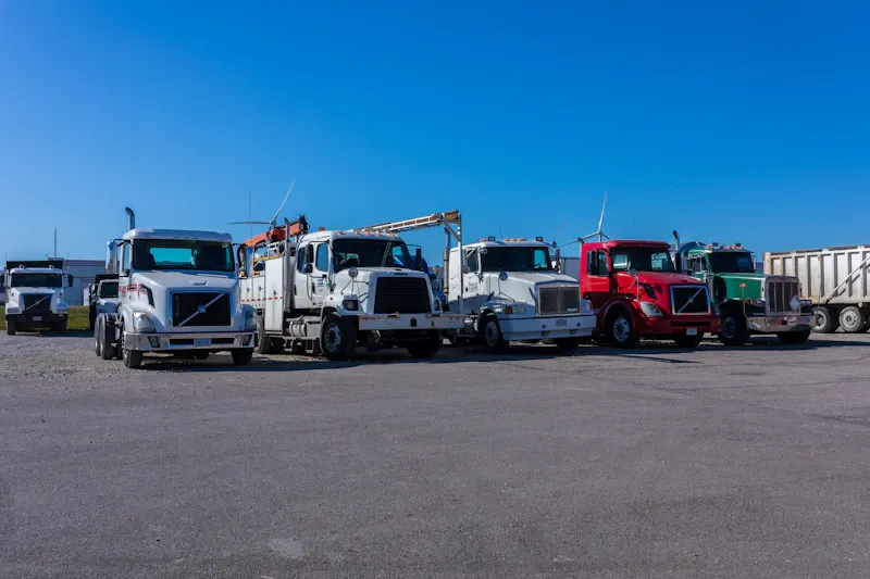 Fleet maintenance for heavy-duty commercial trucks lined up outside a repair facility, including semi-trucks, service trucks, and vocational vehicles.