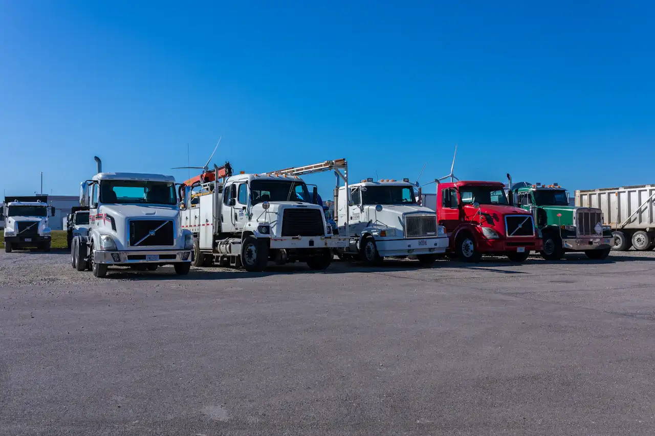 Fleet maintenance for heavy-duty commercial trucks lined up outside a repair facility, including semi-trucks, service trucks, and vocational vehicles.