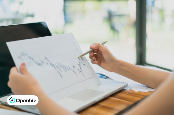 Person pointing at a printed financial line chart next to a laptop, explaining S&P 500 trends