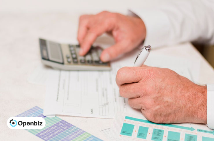 Persona rellenando documentos fiscales con un bolígrafo junto a una hucha y una calculadora sobre un escritorio