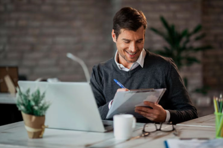 Smiling businessman reviewing documents and working on BCG Matrix analysis with a laptop at his desk.
