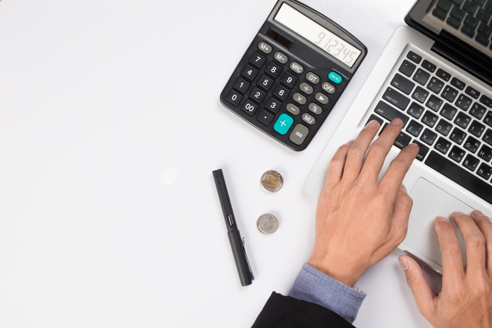 Hands using a calculator and laptop to prepare business taxes and financial reports.