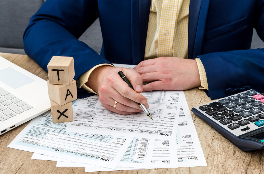 Businessperson completing IRS tax forms with wooden tax blocks and calculator on a desk, symbolizing reporting tax fraud and compliance.