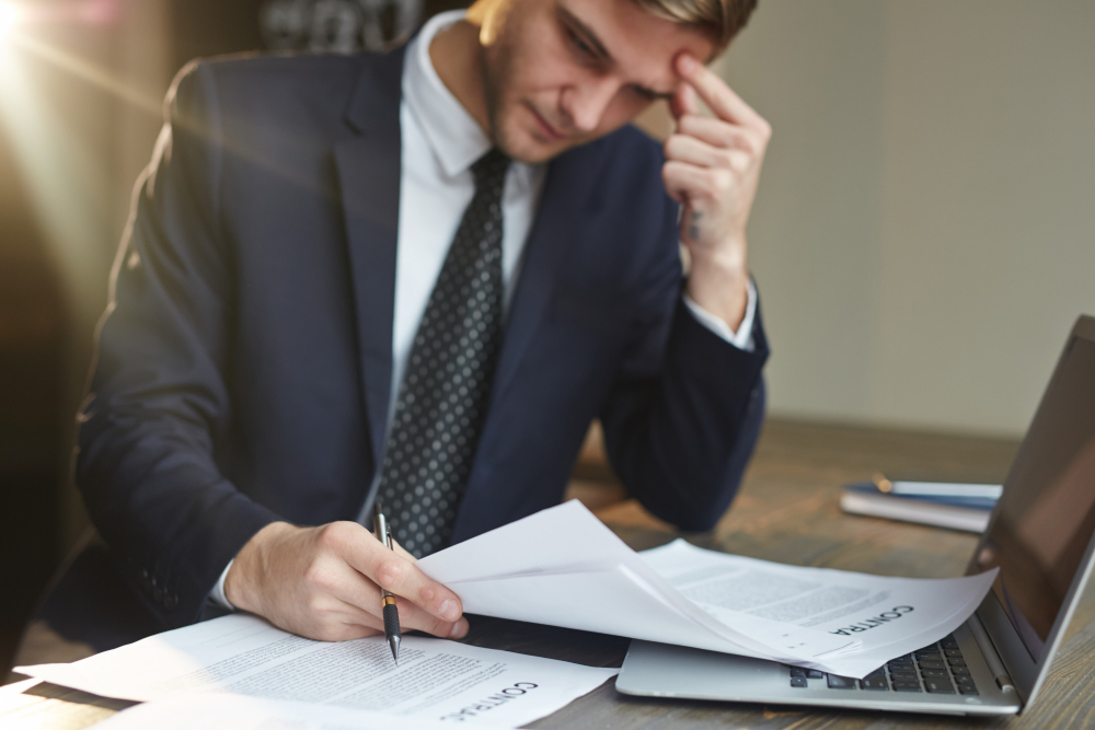 Worried man reviewing tax documents and financial statements, representing the stress and legal risks of not paying business taxes.