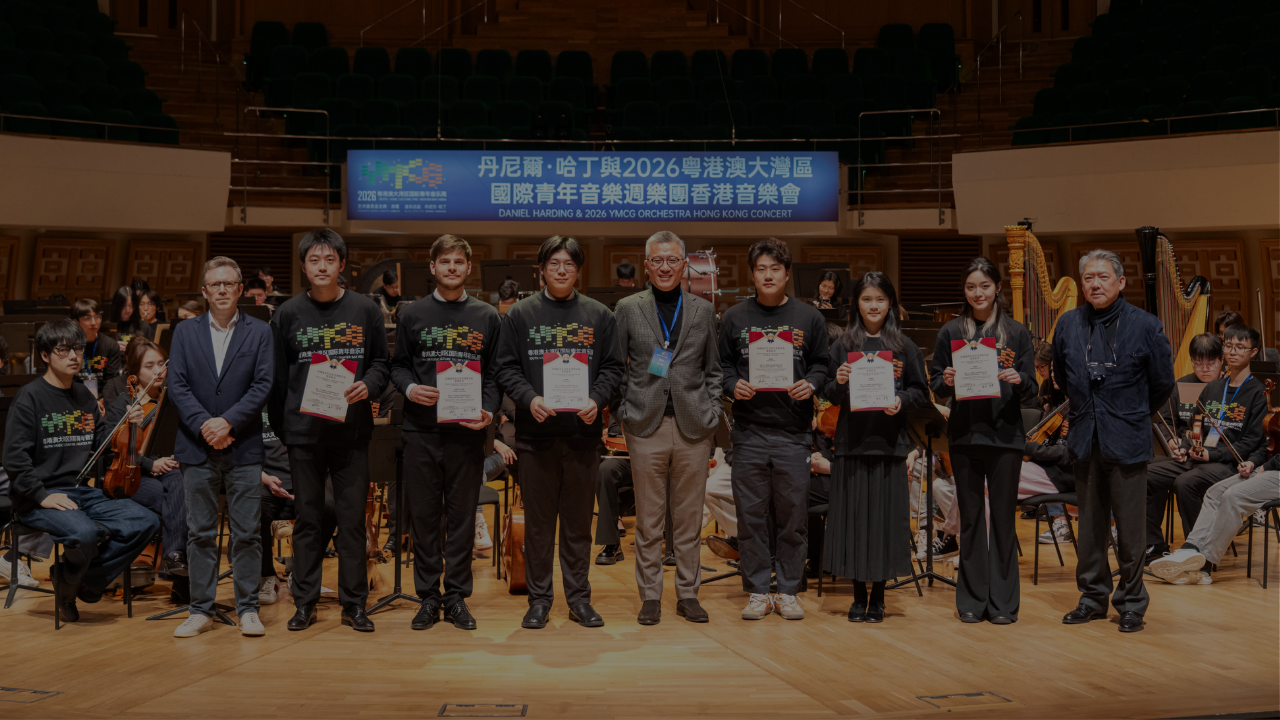 Group of musicians on stage holding certificates with donor Mr. Steven Ying in 2026 YMCG Orchestra Hong Kong concert.