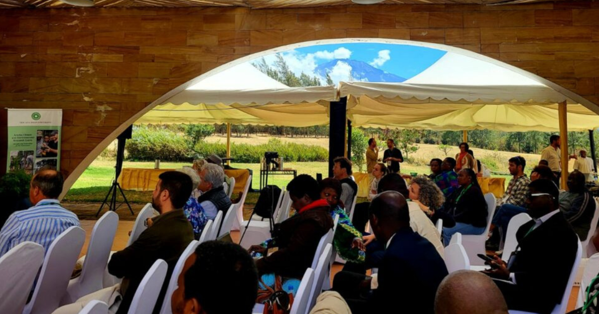 Audience seated under a large tent with a scenic view of Mount Meru, Arusha, Tanzania, during an outdoor event.