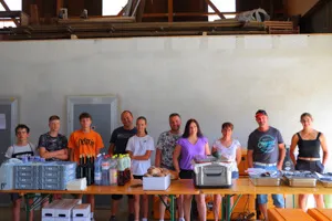 Dix personnes debout derrière une table couverte de boîtes, bouteilles et articles emballés dans un espace intérieur.