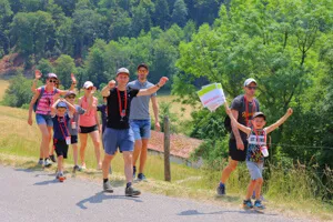 Un groupe de personnes de différents âges fait de la randonnée sur une route de campagne, un garçon tenant un drapeau avec le mot Raiffeisen.