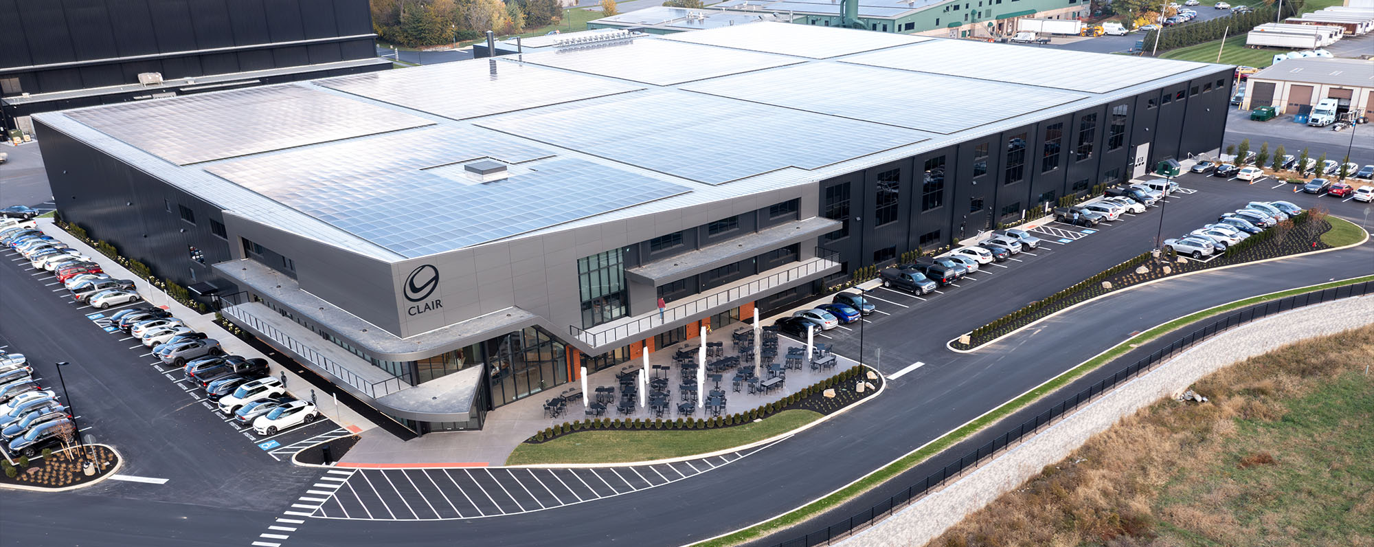 A drone shot of Clair Global's headquarters. a large grey and black building with lots of big windows and solar panels on the roof