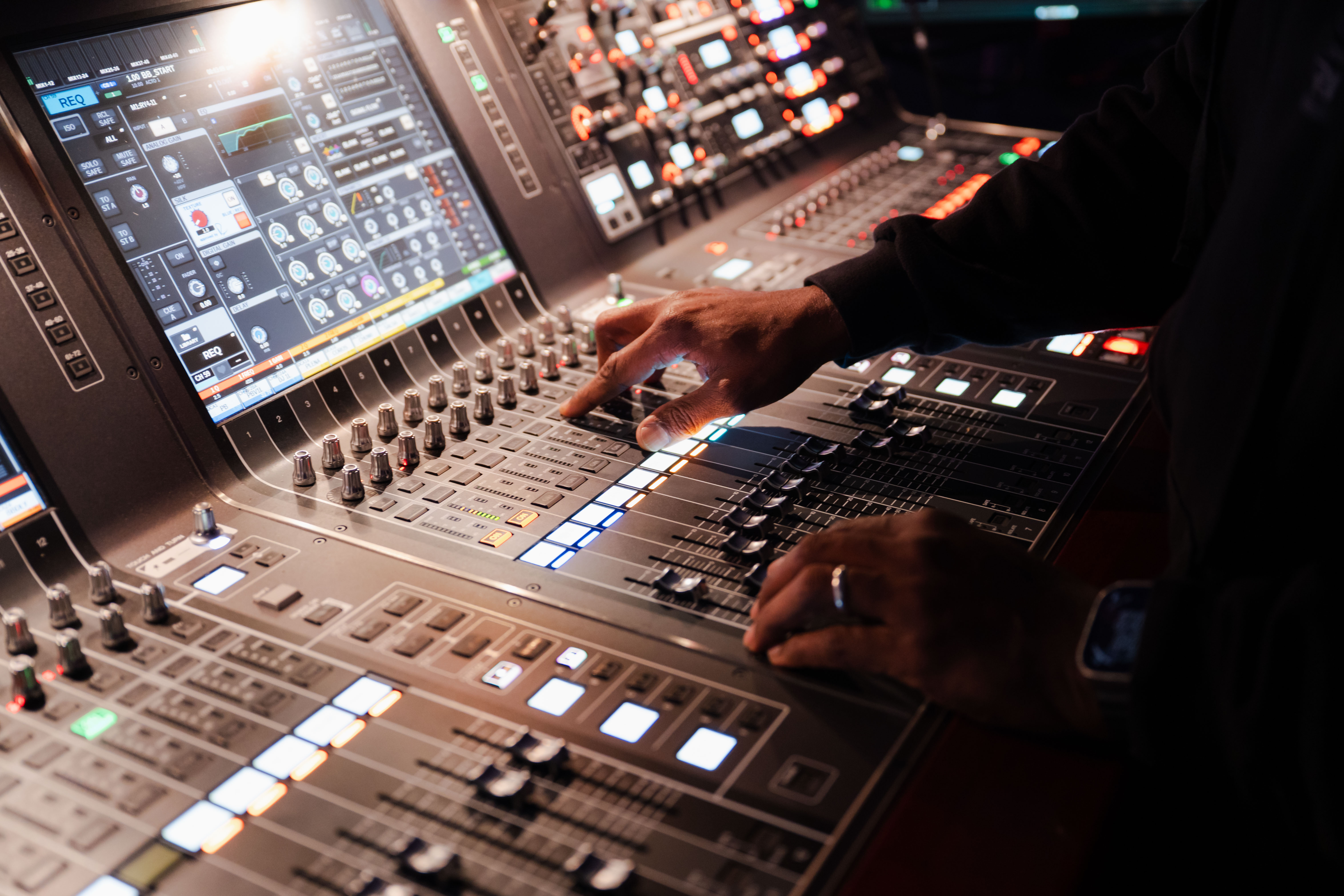 A close up of José Rivera's hands pushing faders on a console