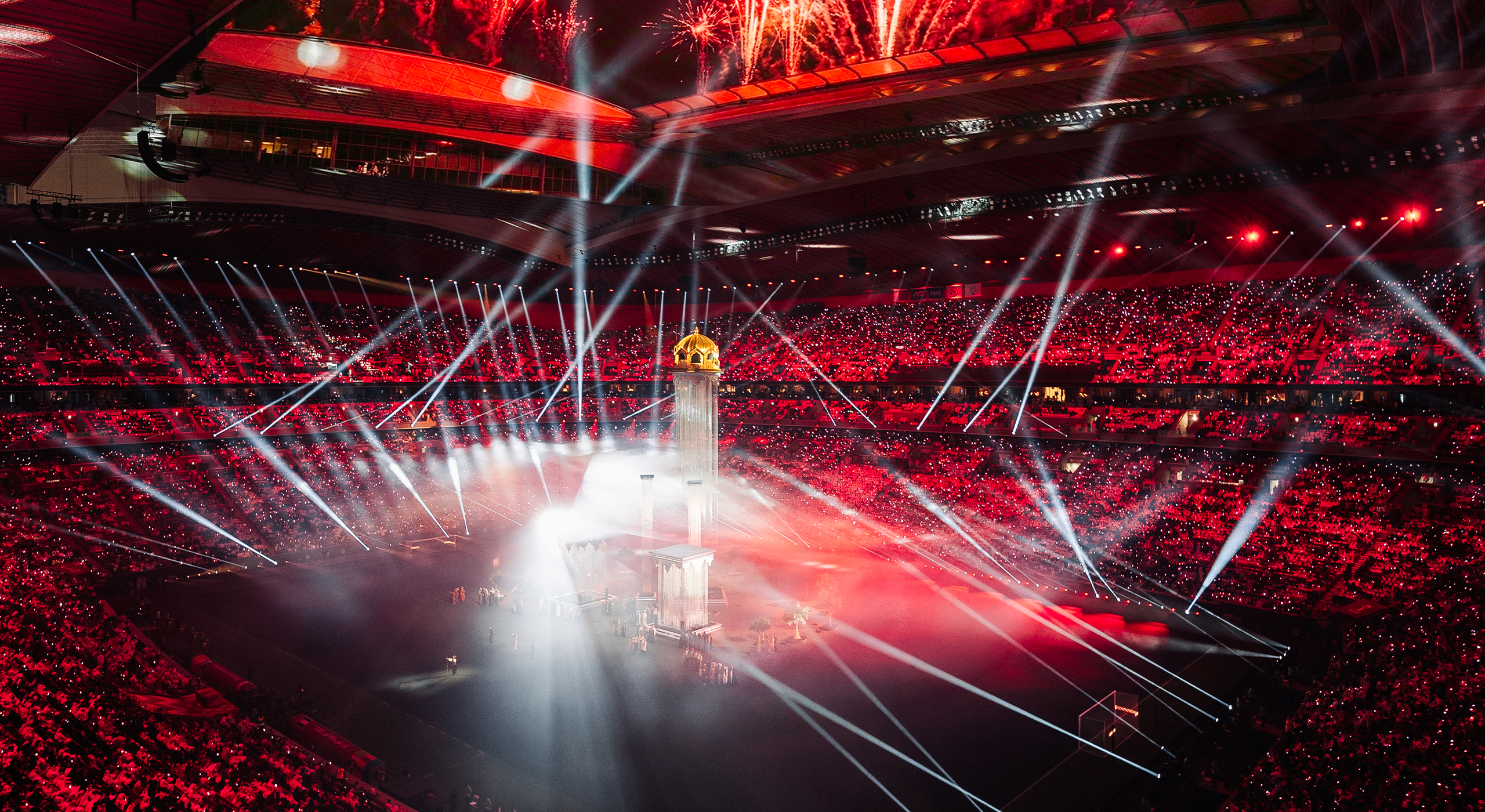 A wide shot of a packed stadium with beams of light shining down on an ornate set and performers at the Arab Cup Opening Ceremony