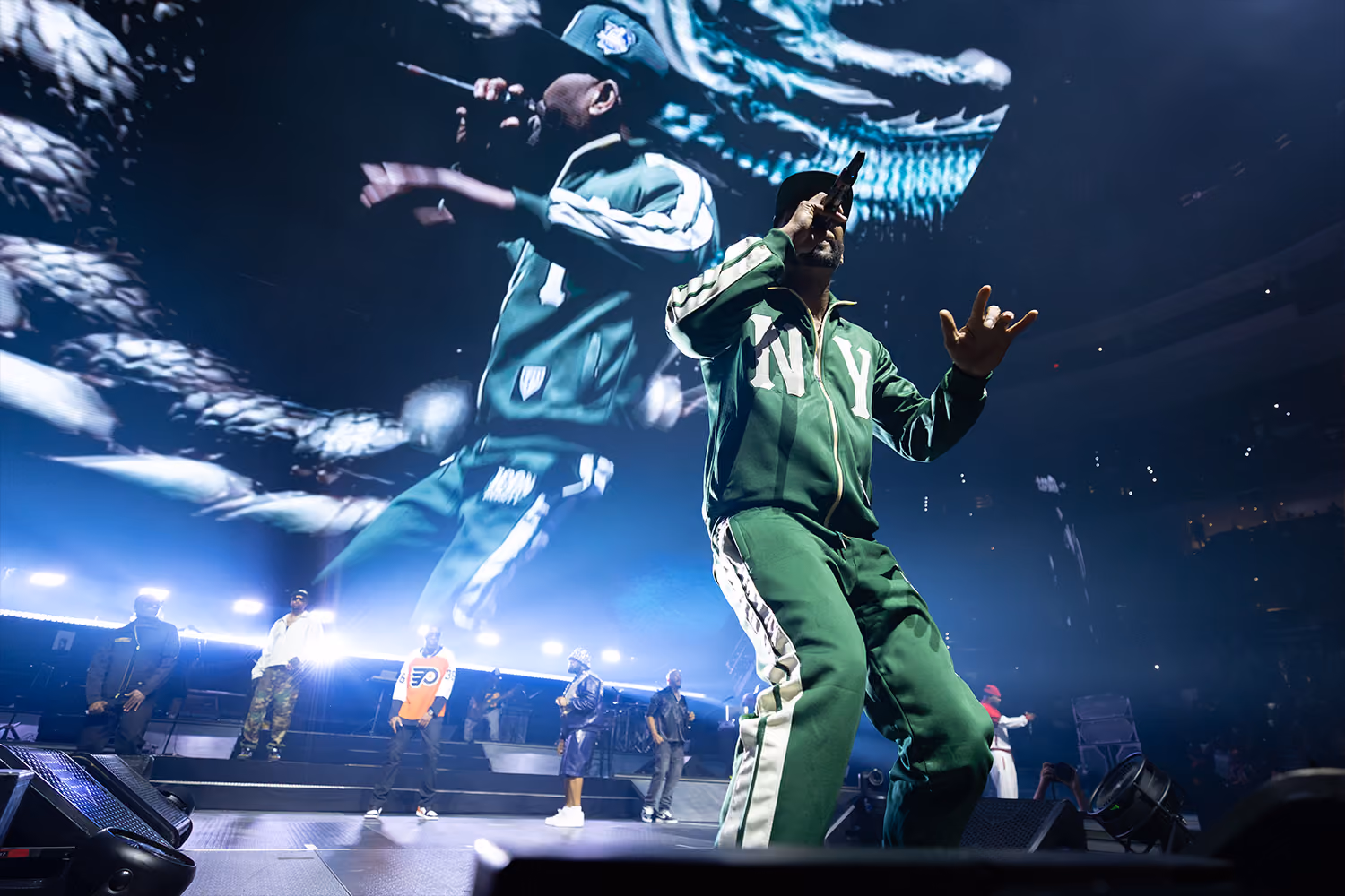 A close up of RZA, wearing a green New York sweatsuit, rapping at a Wu-Tang concert