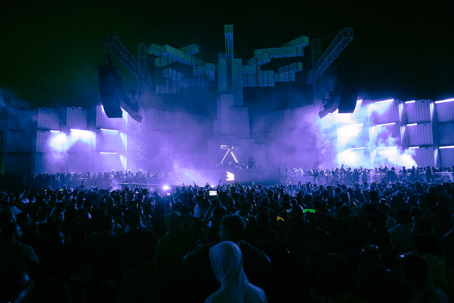 "Enthusiastic concertgoers at MDLBeast Soundstorm, immersed in vibrant purple lights and a striking geometric stage design