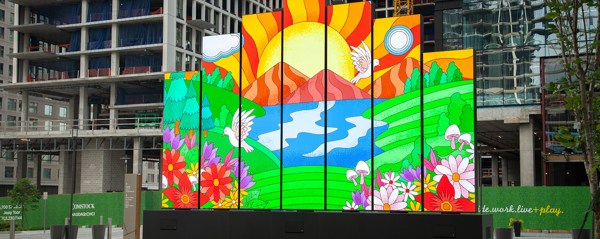 An installation of a series of LED panels staggered displaying a colorful illustration of the sun and grass are displayed