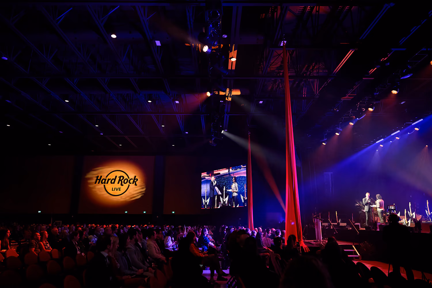 A crowd watching a presenter on a stage with blue lights at Hard Rock Ottawa