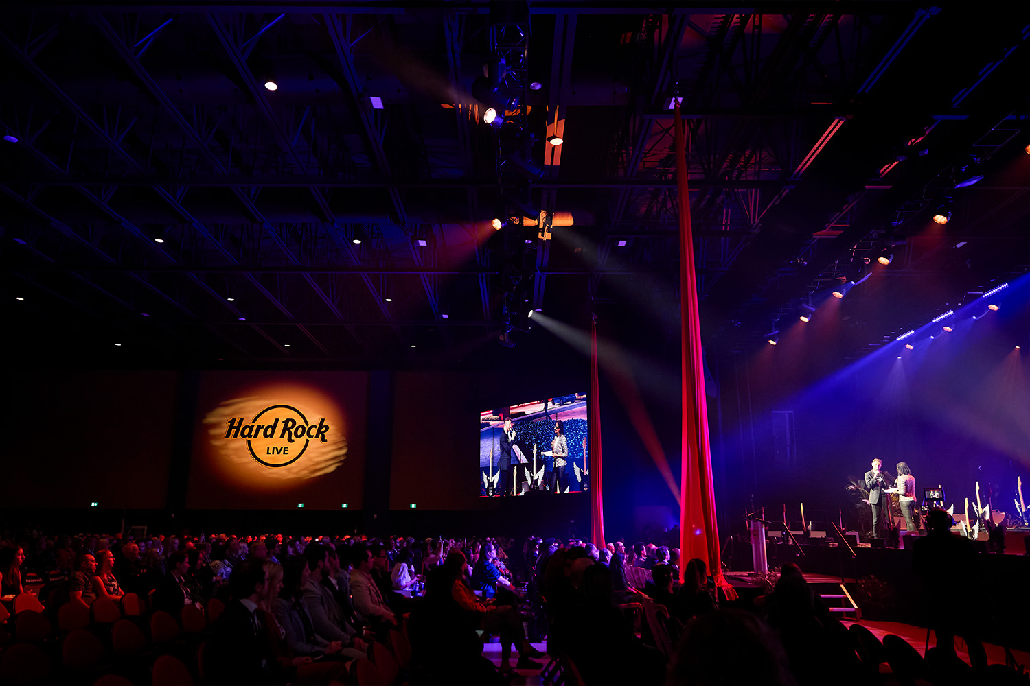 A crowd watching a presenter on a stage with blue lights at Hard Rock Ottawa