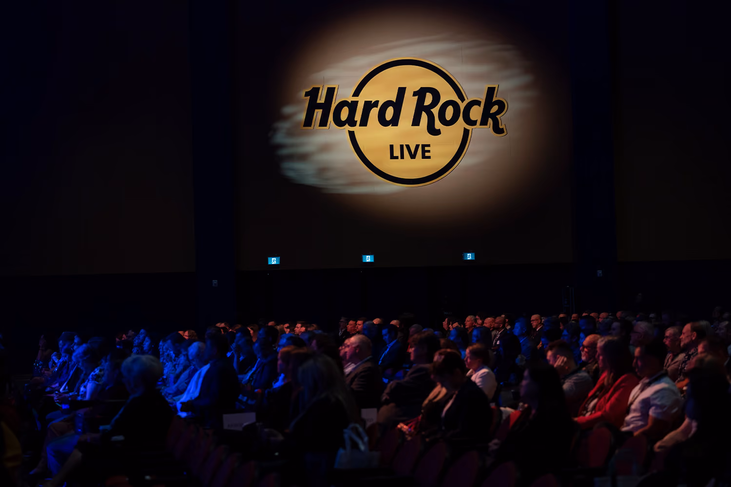 A crowd in a dark space with a Hard Rock Live sign illuminated on the wall behind them