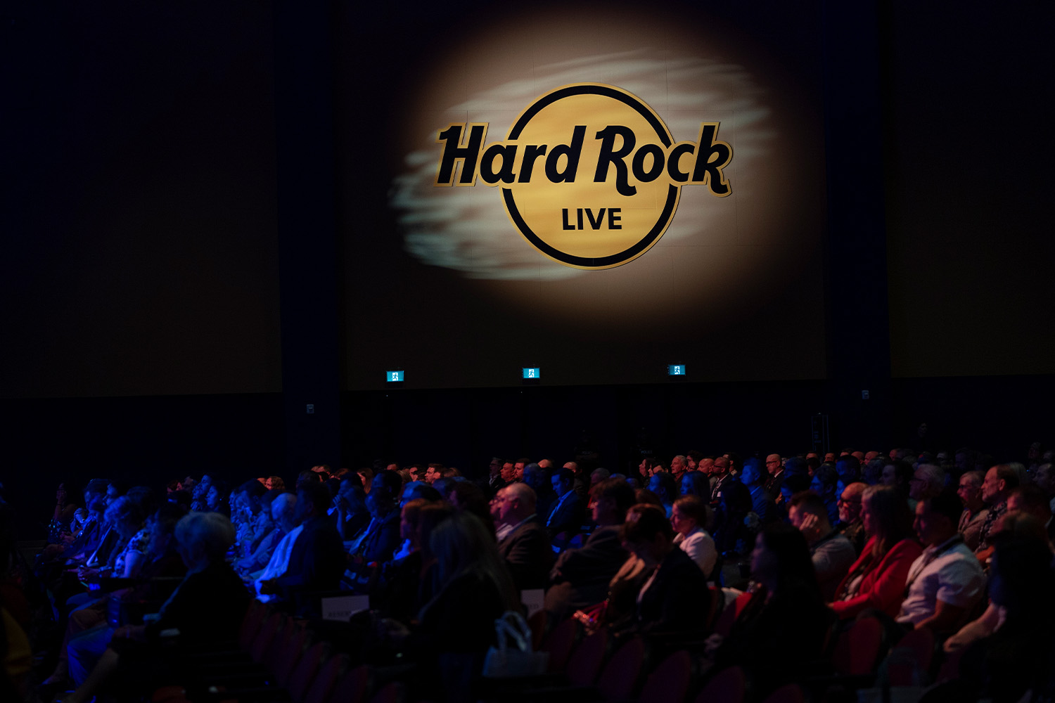 A crowd in a dark space with a Hard Rock Live sign illuminated on the wall behind them