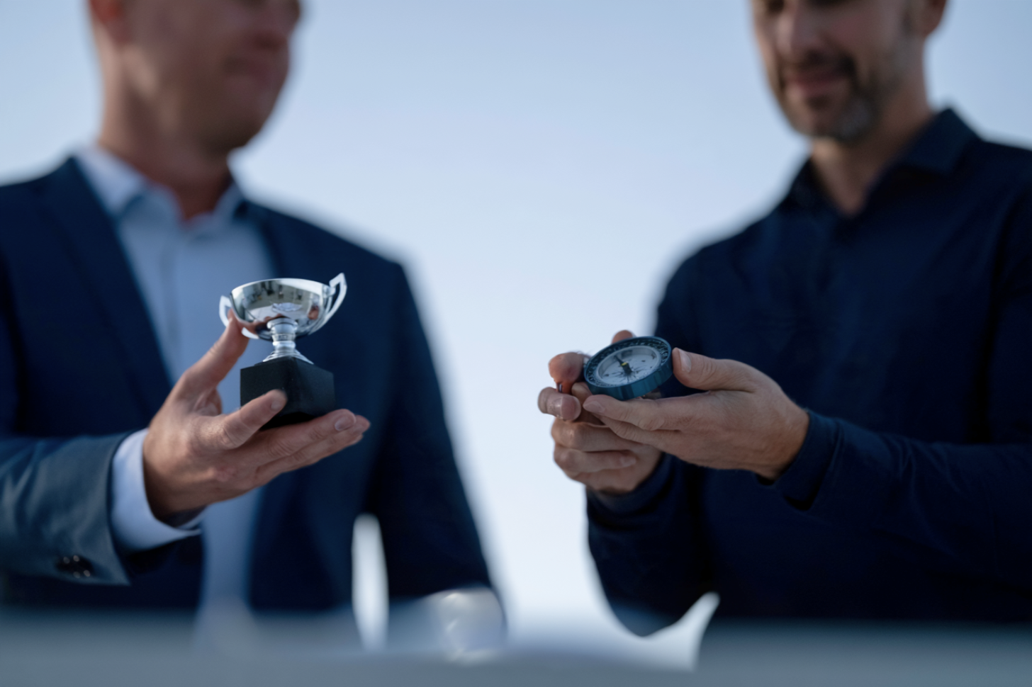 Two people side by side — one holding a trophy, the other holding a compass — representing past performance versus future potential.