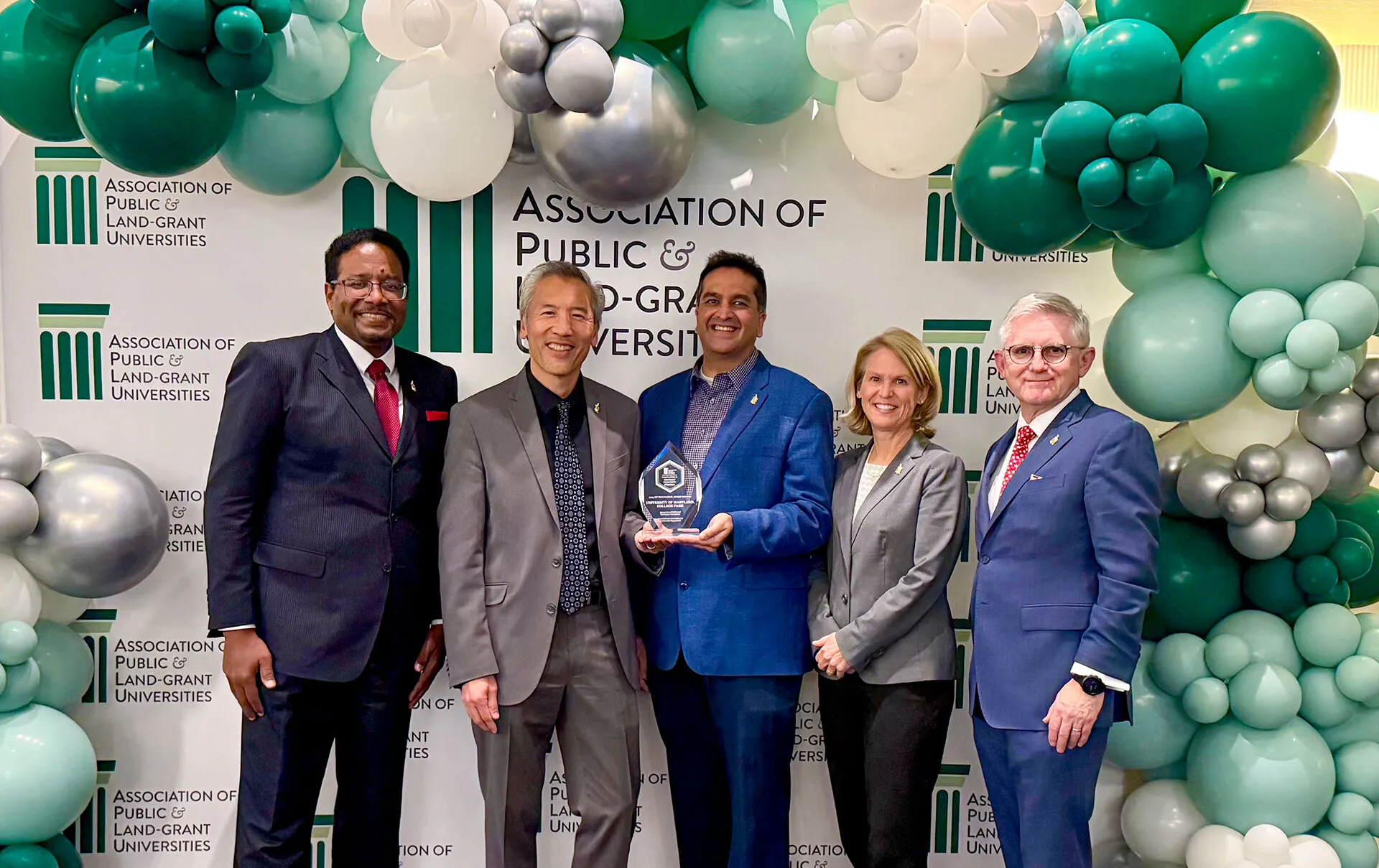 five university leaders pose with award under green and white balloons