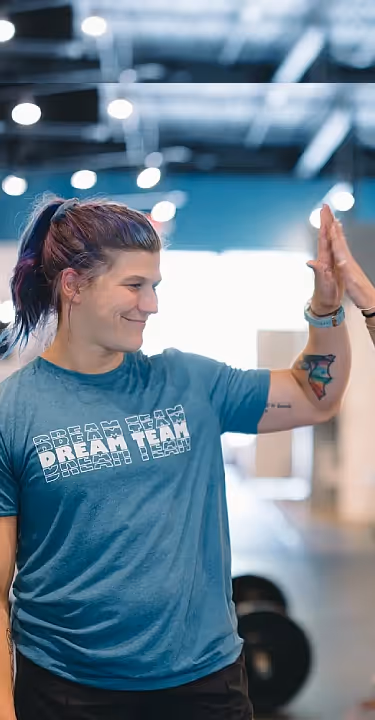 A female coach in a CrossFit gym in Atlanta, GA assists an athlete with a bar exercise, emphasizing proper form and technique.