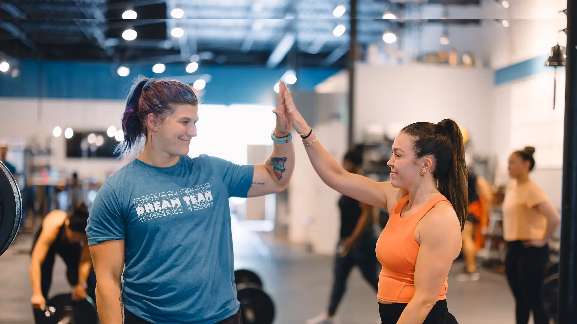 A female coach in a CrossFit gym in Atlanta, GA assists an athlete with a bar exercise, emphasizing proper form and technique.
